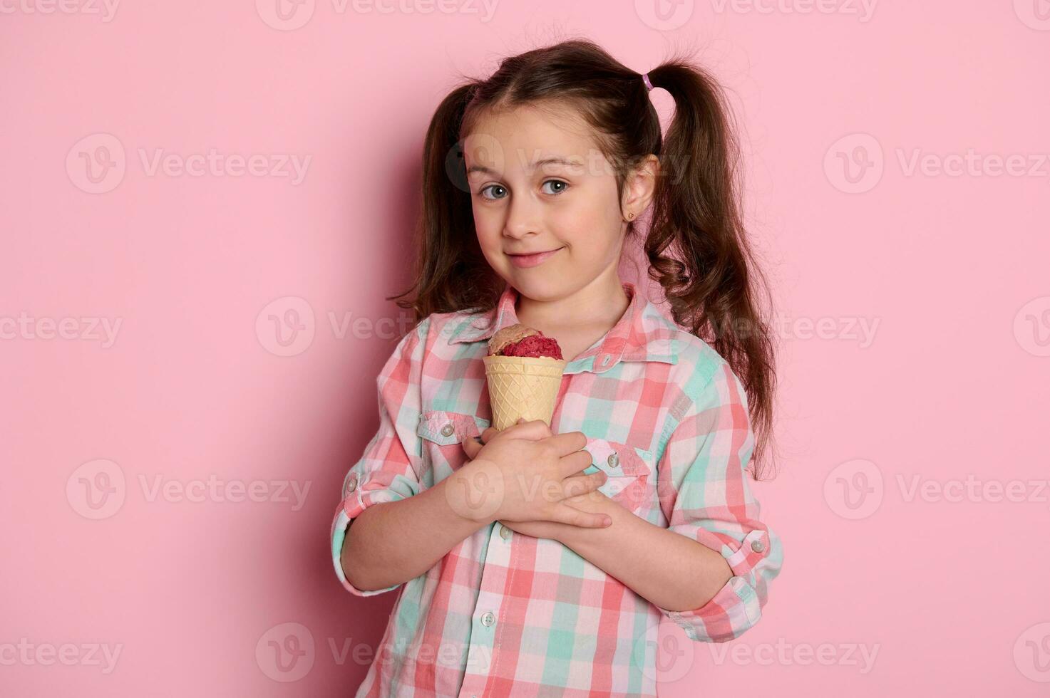 adorável criança menina detém uma waffle cone com chocolate morango gelo creme, sorrisos olhando às Câmera, isolado em Rosa foto