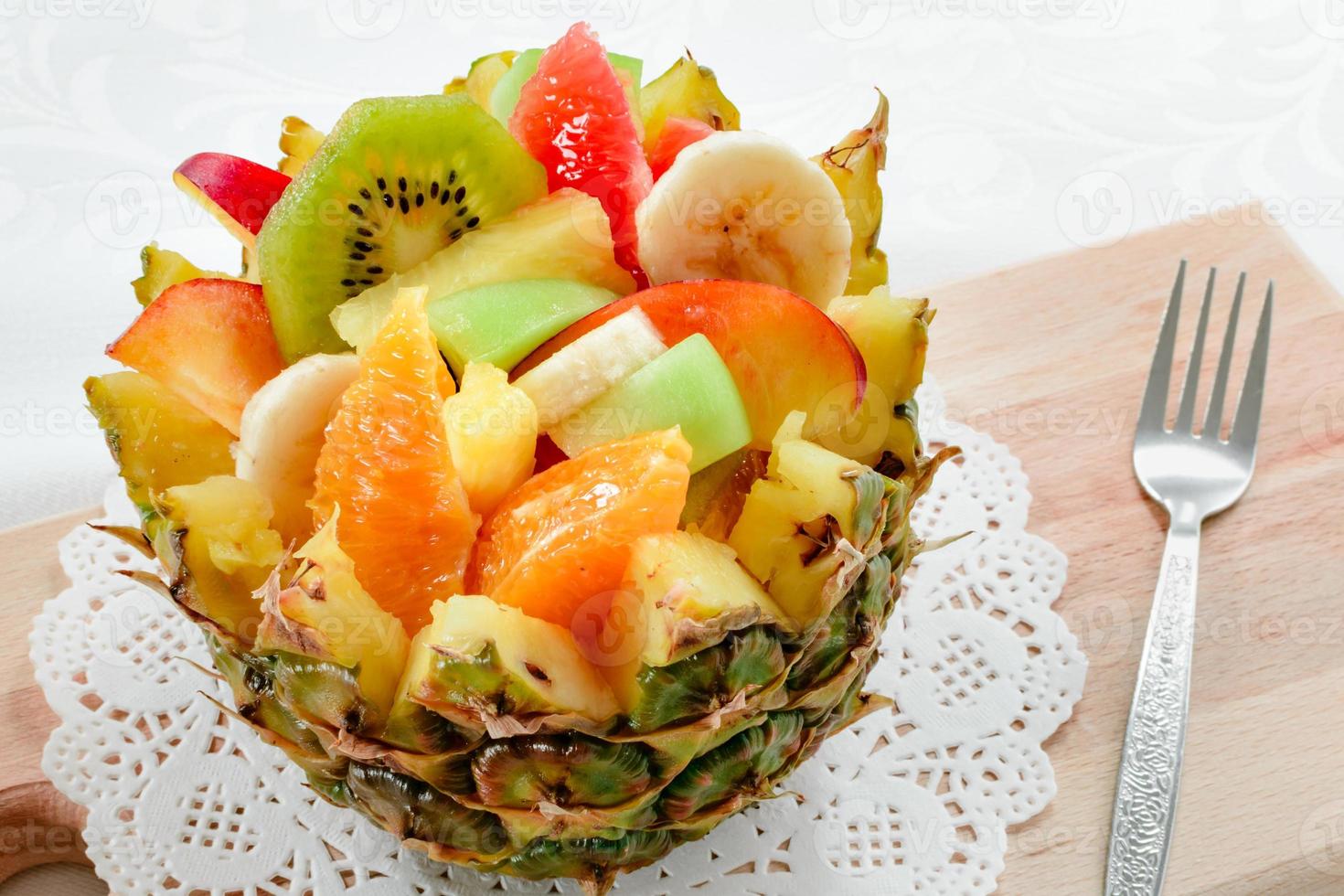 Salada de frutas frescas com kiwi, banana, pêssego, laranja, laranja vermelha, damasco e melão em tigela de abacaxi artesanal. foto