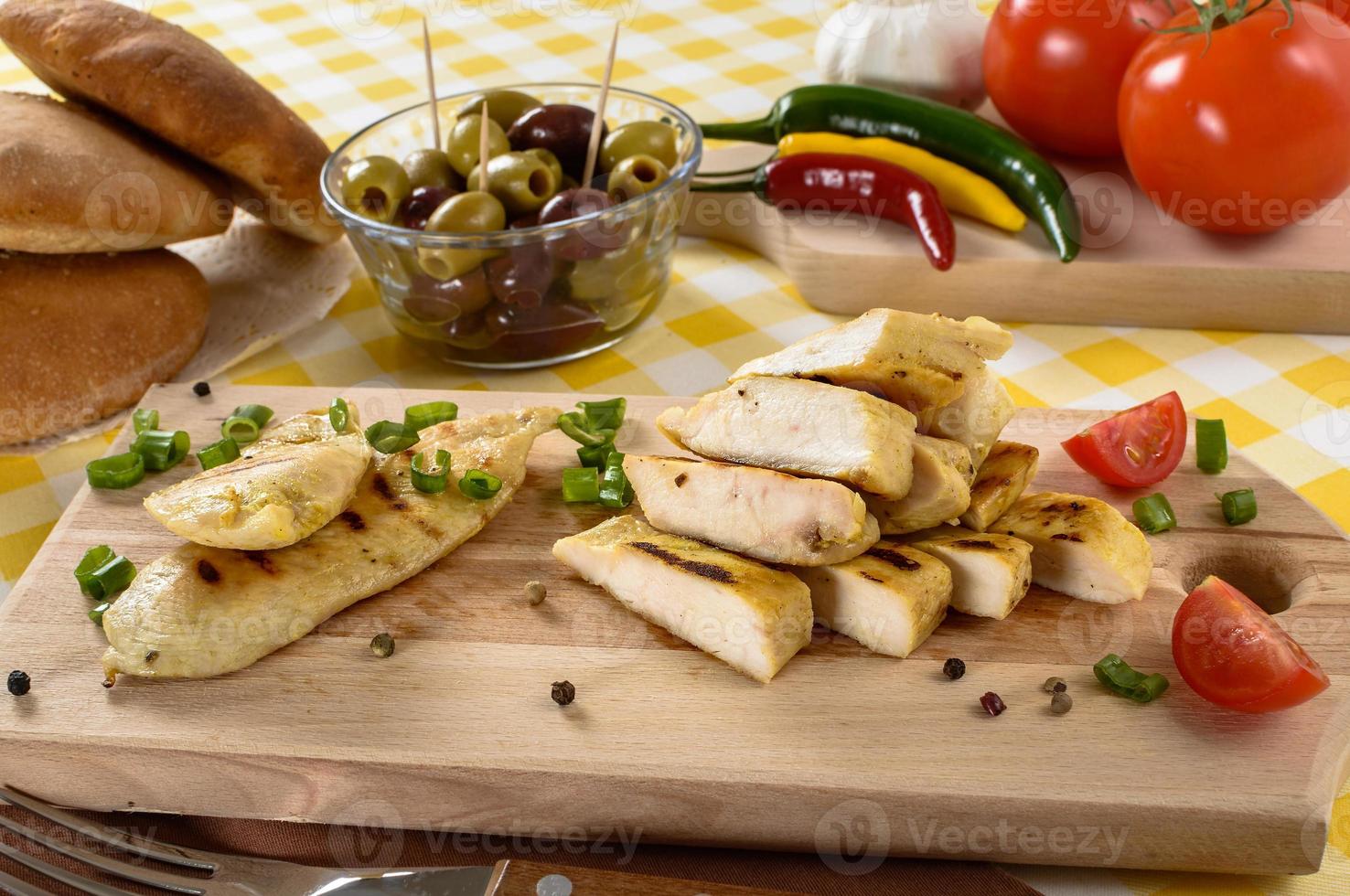 Carne de frango grelhado na placa de madeira com legumes e azeitonas no fundo. foto