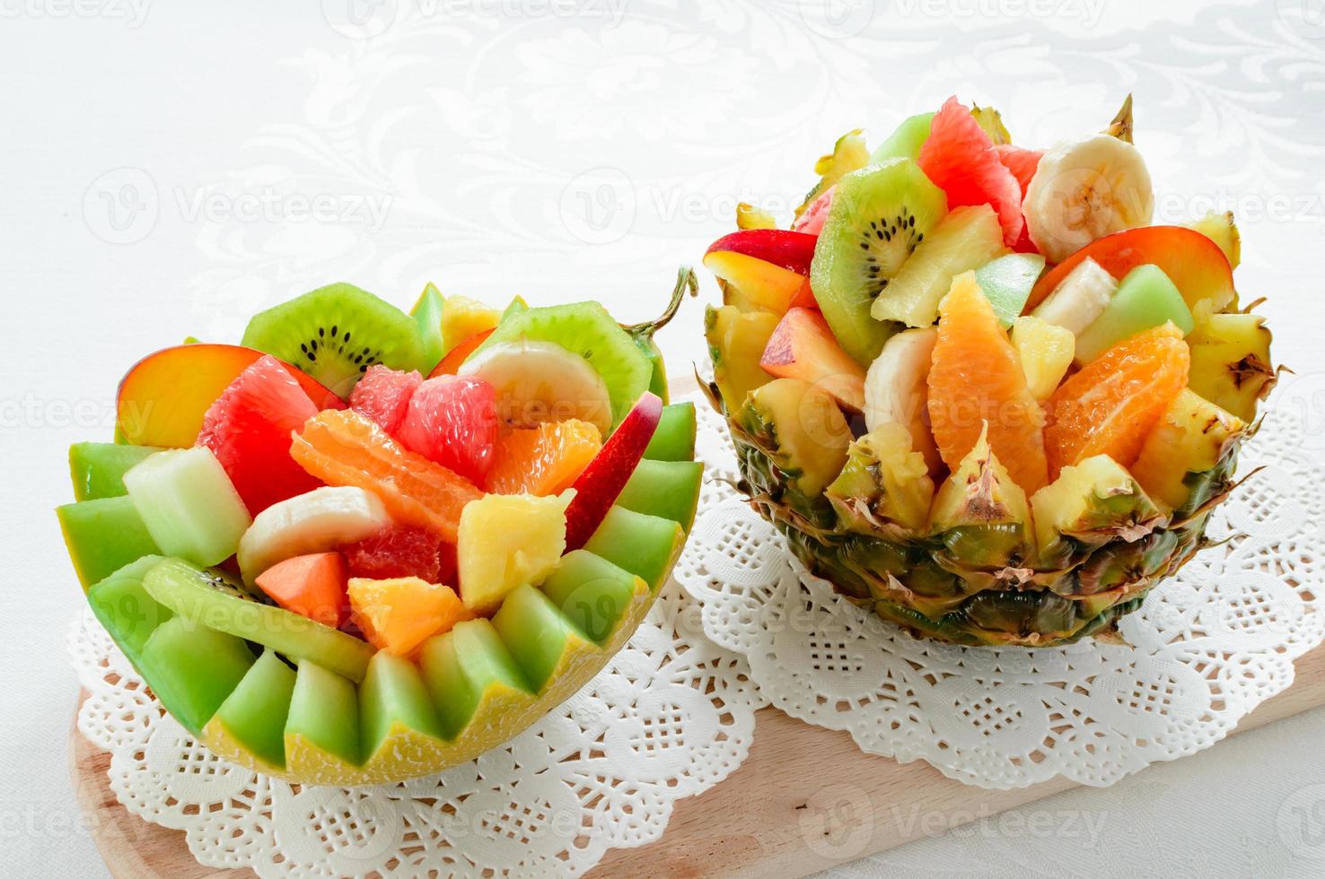 duas salada de frutas frescas com kiwi, banana, pêssego, laranja, laranja vermelha, damasco e melão em tigela de melão e abacaxi artesanal. foto