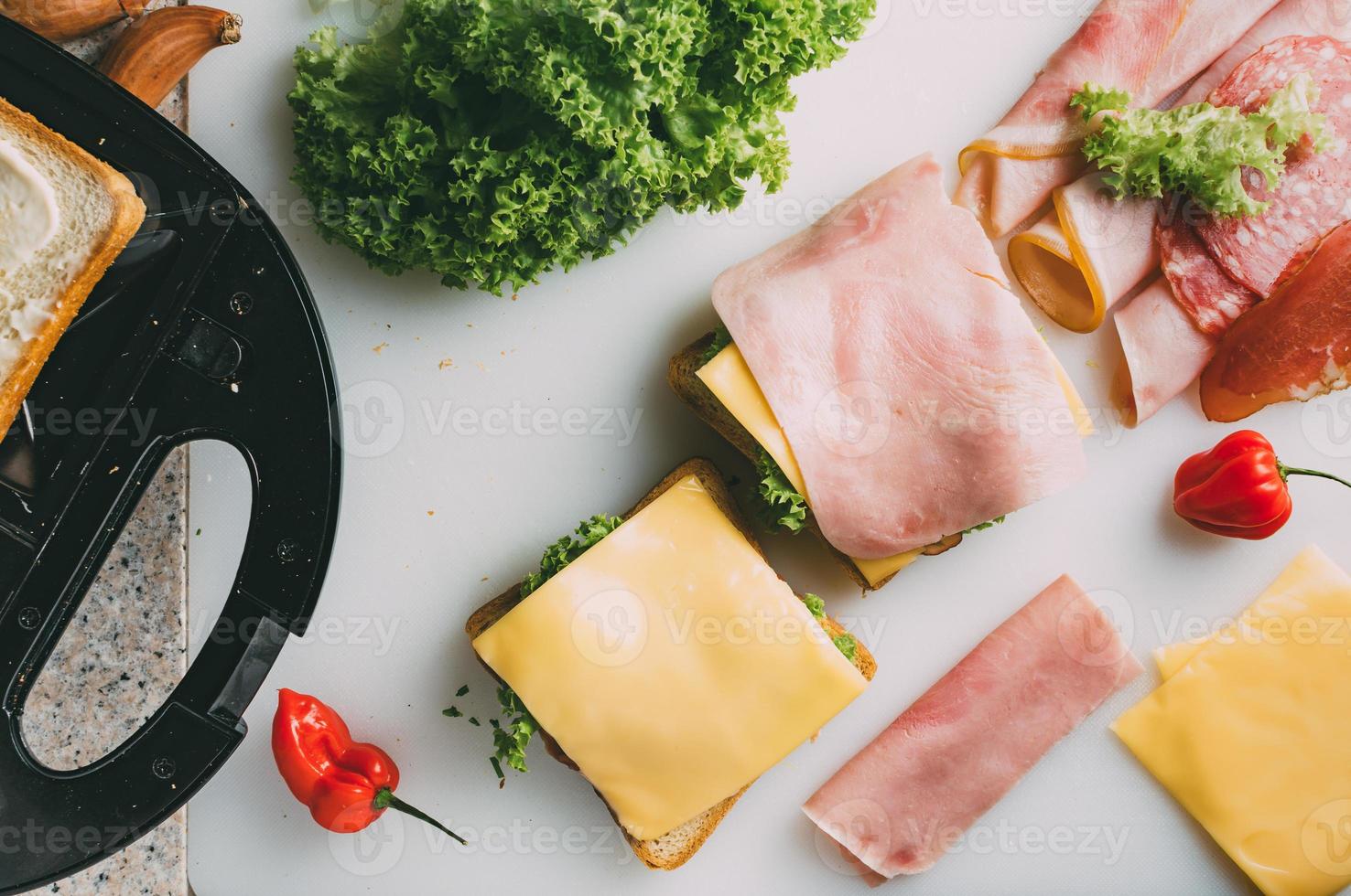 sanduíche club com presunto, salame, carne defumada, queijo, alface e rúcula. preparação de sanduíches de torradas. vista do topo. foto