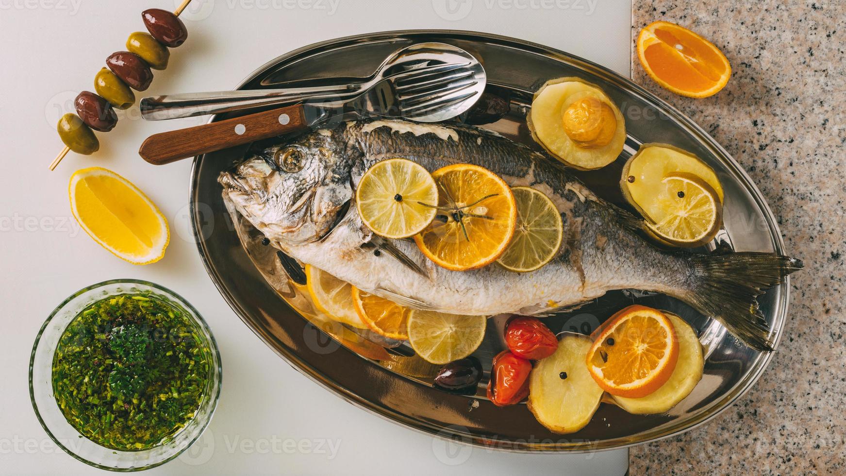 Peixe dourado do mar no prato assado com batata, alecrim, limão, laranja, azeitonas, tomate e lima. orata fresco, preparação de peixe dorade. foto