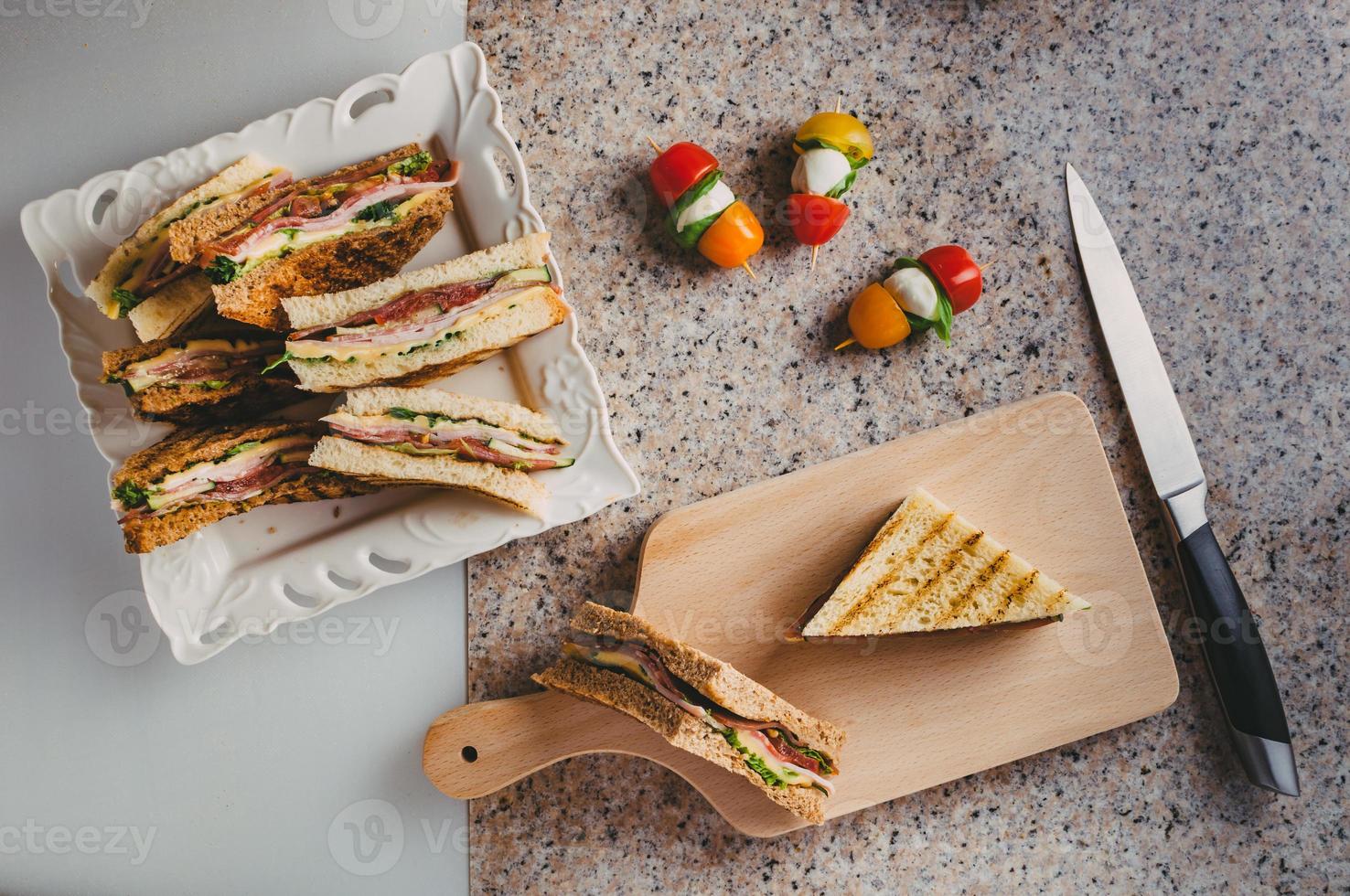 sanduíche club com presunto, salame, carne defumada, queijo, alface e rúcula. Preparação de sanduíche de torrada. foto