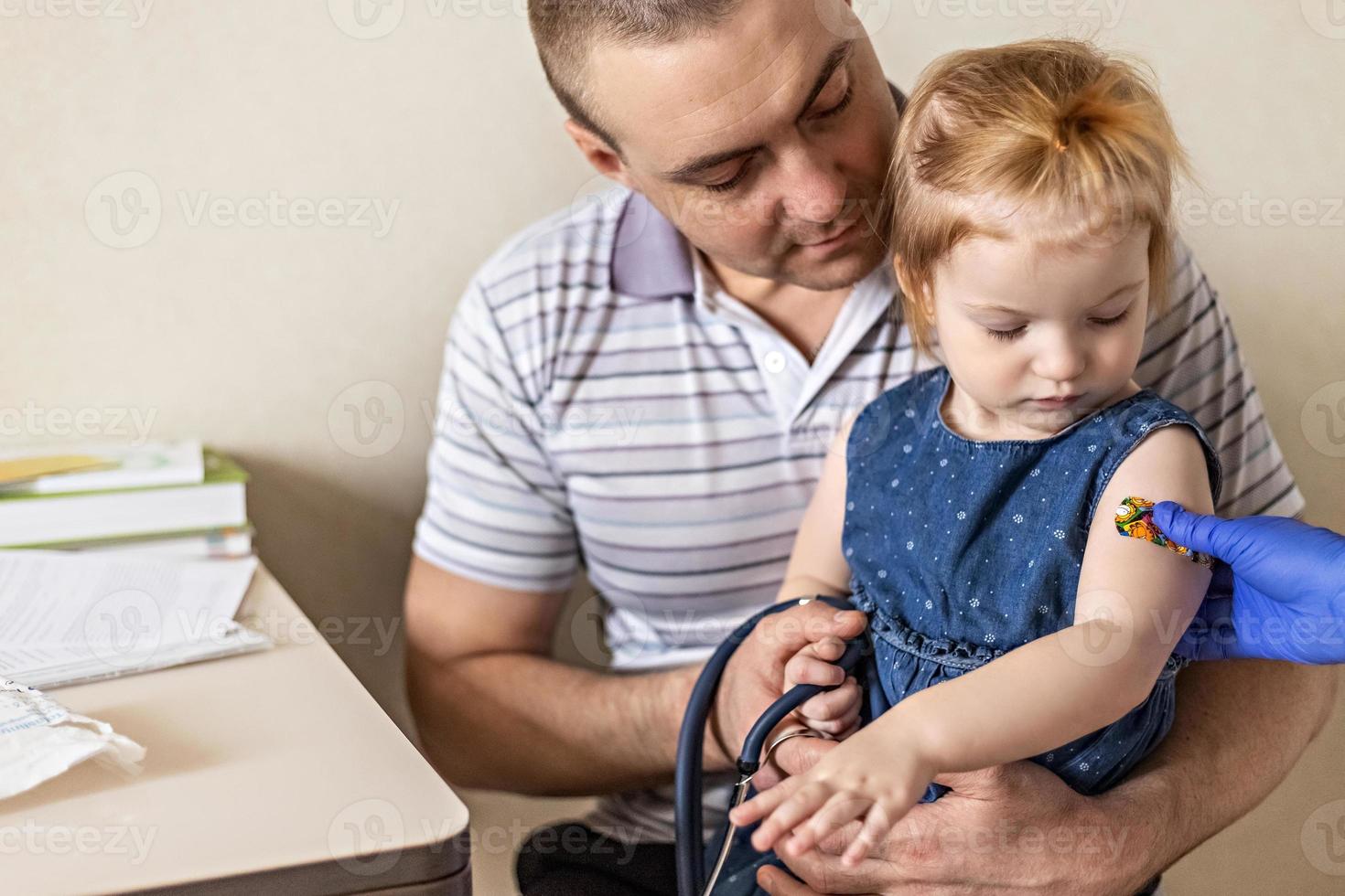 vacinação de uma menina nos braços do pai no consultório do médico contra o coronavírus. gesso adesivo engraçado infantil. vacina contra covid-19, gripe, doenças infecciosas. foto