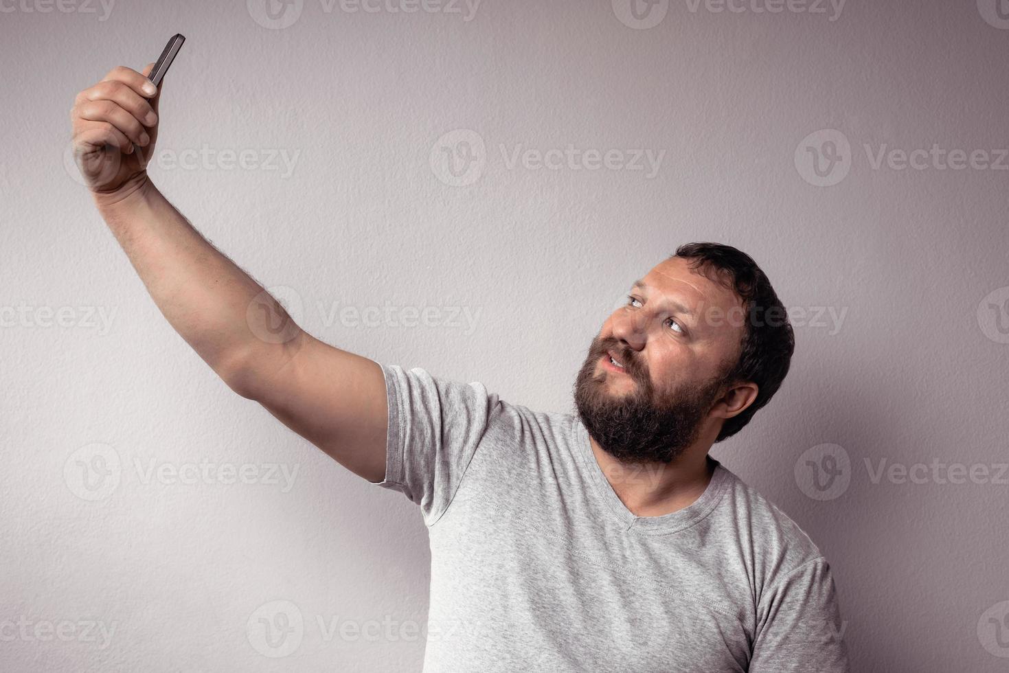 bonito homem barbudo em camiseta cinza olhando para o smartphone foto