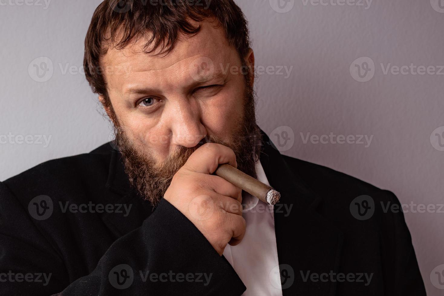 homem barbudo com casaco e camisa modernos fumando seu charuto foto