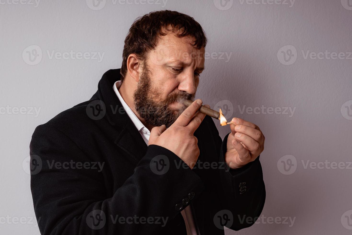 homem barbudo com casaco e camisa modernos acendendo o charuto foto