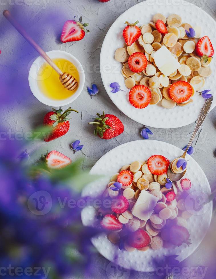 Cereais para panqueca, comida da moda. mini panquecas de cereais com manteiga, mel e morangos. foto