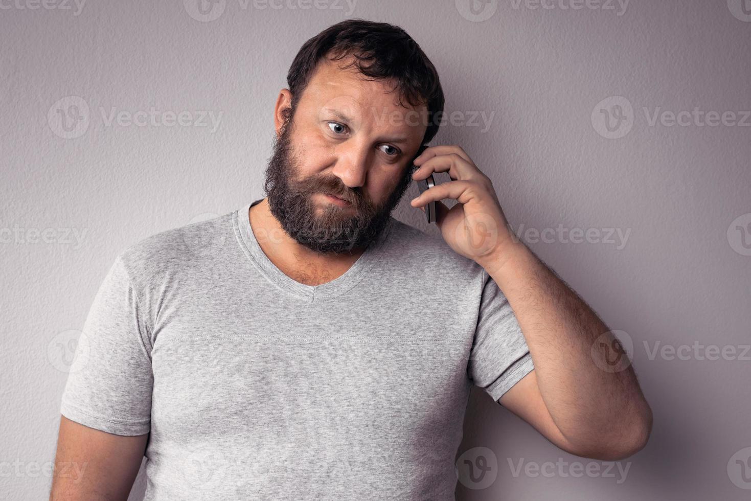 homem barbudo de camiseta cinza segurando um telefone celular foto