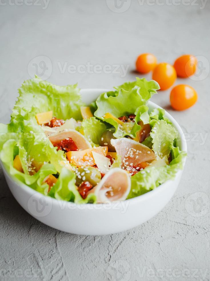 salada fresca de alface, tomate cereja, azeitonas, tomates secos ao sol, presunto de parma, queijo cheddar, parmesão, azeite e gergelim. conceito de alimentação saudável. foto