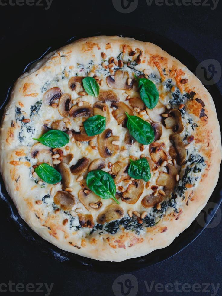 pizza caseira com cogumelos, espinafre, alho, cream cheese e pinhões, sobre um fundo escuro. foto