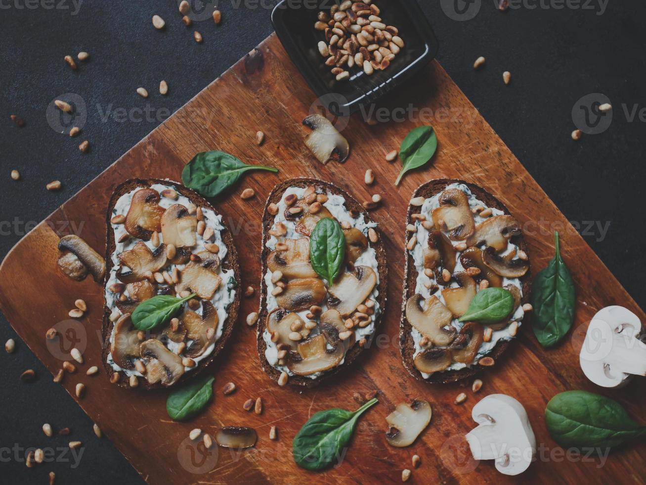 saborosa bruschetta fresca com cogumelos, espinafre, alho, cream cheese e pinhões, em uma placa de madeira, sobre um fundo escuro. foto