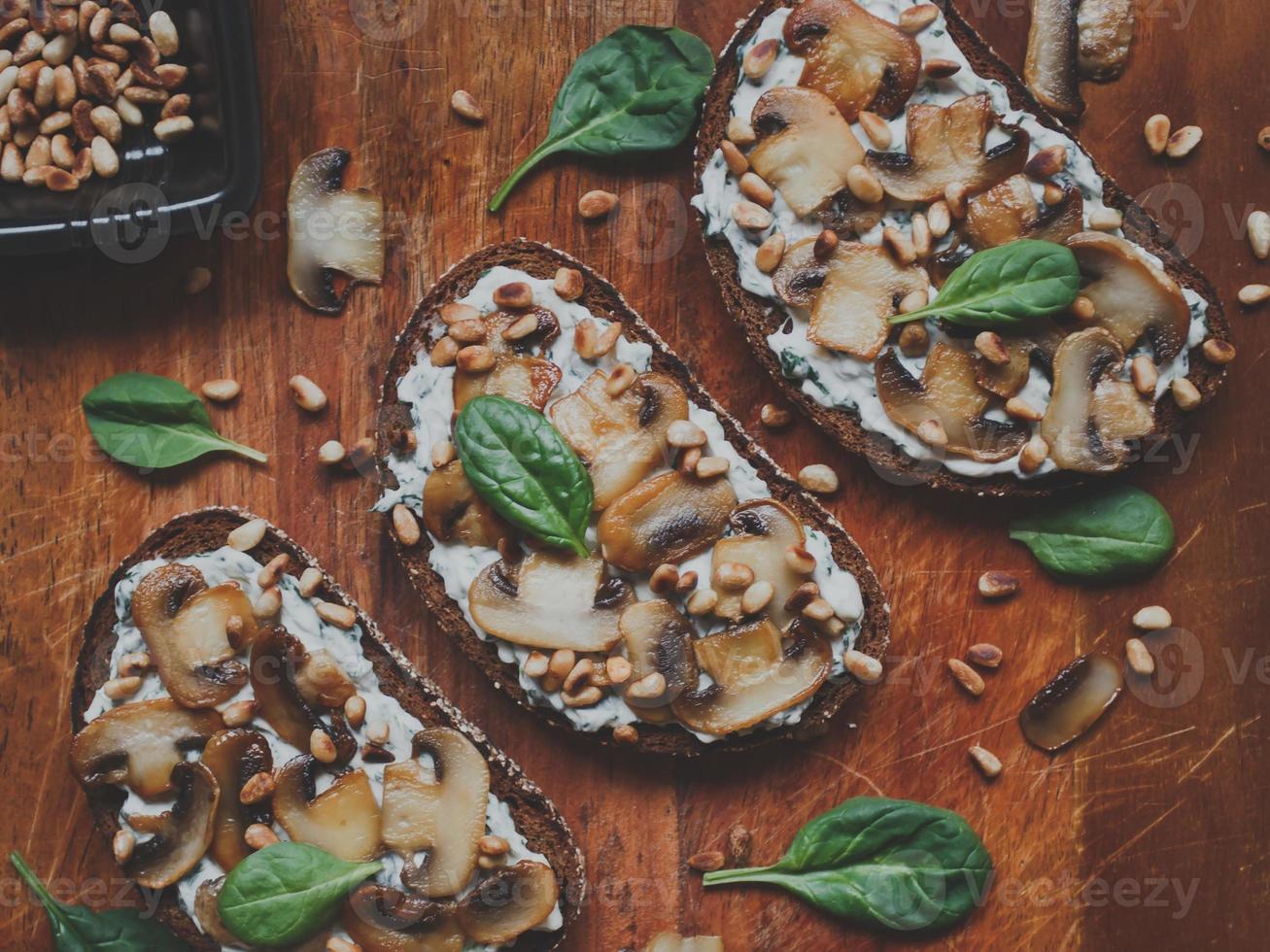 saborosa bruschetta fresca com cogumelos, espinafre, alho, cream cheese e pinhões, em uma placa de madeira, sobre um fundo escuro. foto