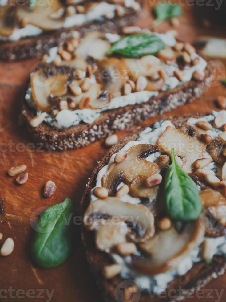 saborosa bruschetta fresca com cogumelos, espinafre, alho, cream cheese e pinhões, em uma placa de madeira, sobre um fundo escuro. foto