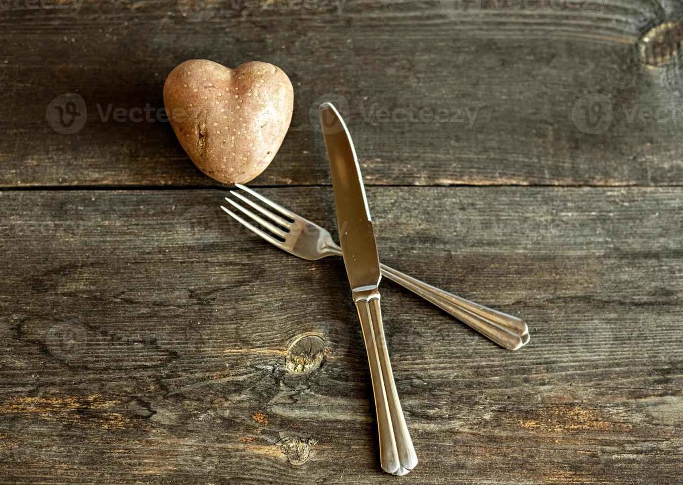 batatas vermelhas em forma de um coração em um fundo de madeira com um garfo e uma faca. o conceito de agricultura, colheita, vegetarianismo. Dia dos Namorados. comida quadrada e feia. foto