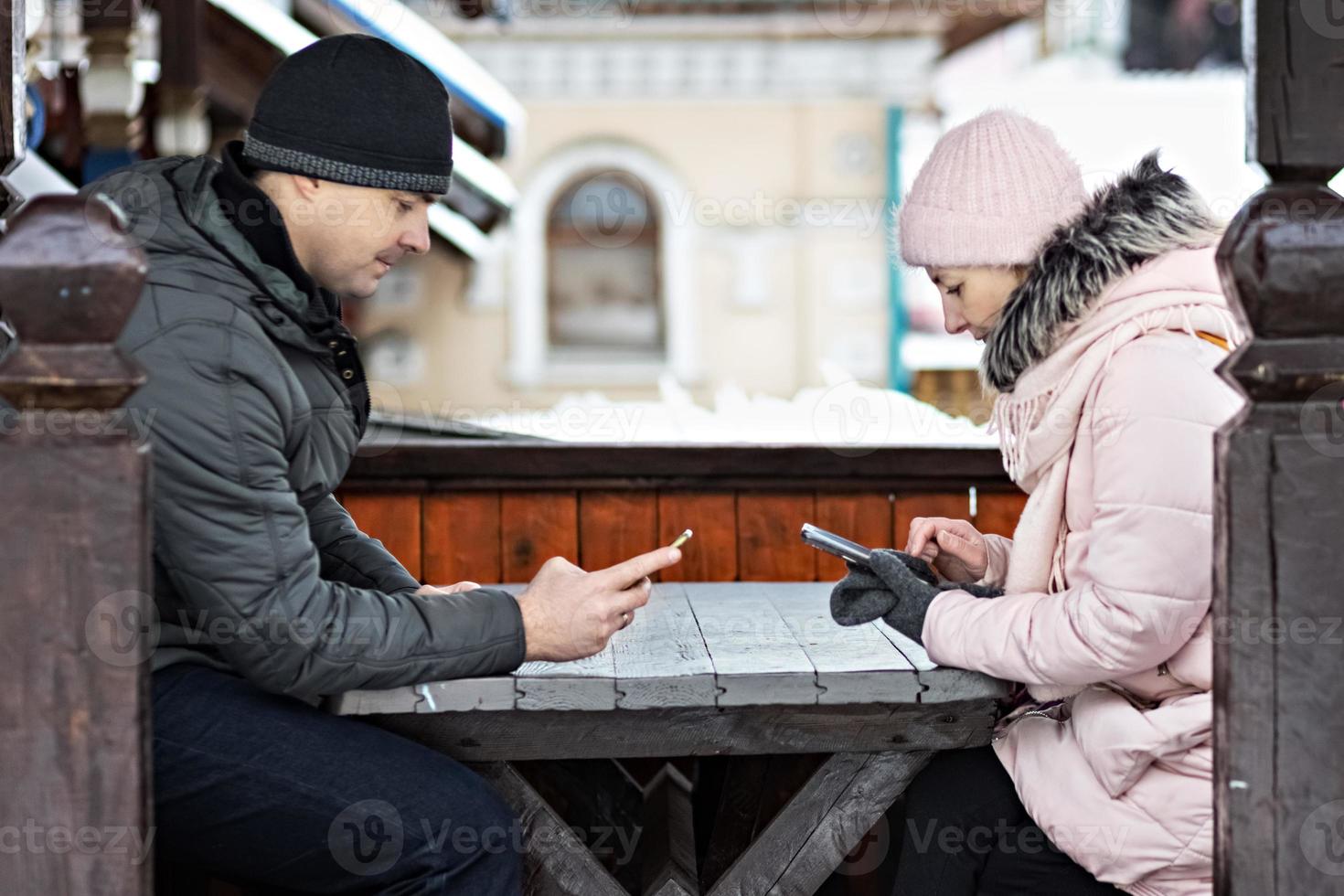 um casal está esperando o pedido do almoço em um café de rua, enviando mensagens de texto por telefone. comunicação com pessoas em um smartphone. foto