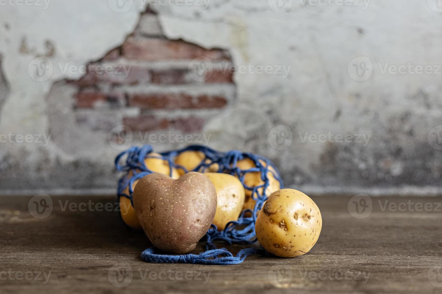 Batatas vermelhas em forma de coração com batatas brancas em uma eco-grade azul em um close-up de fundo de madeira foto