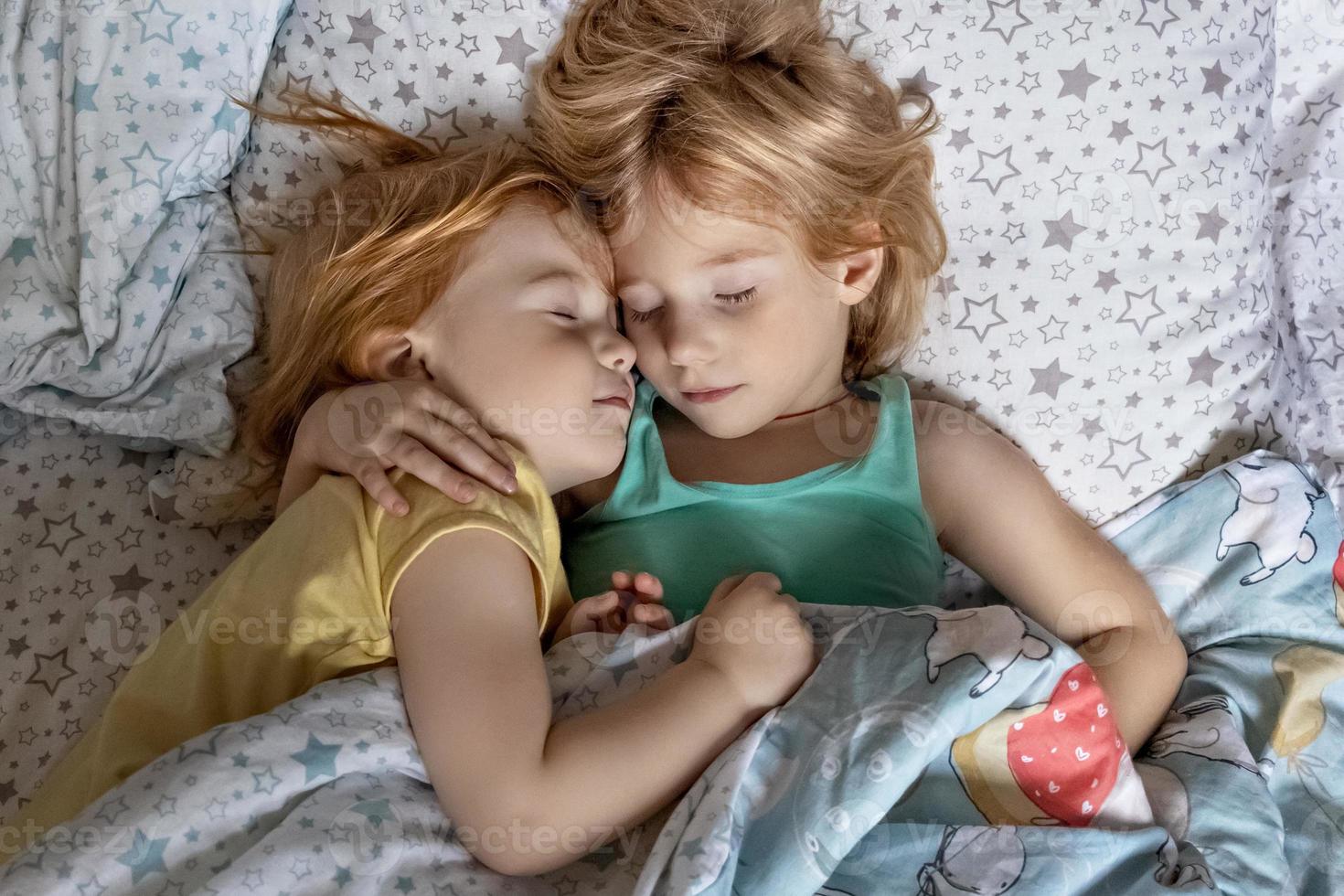 duas irmãzinhas irmãs dormindo em um abraço na cama sob o mesmo cobertor foto