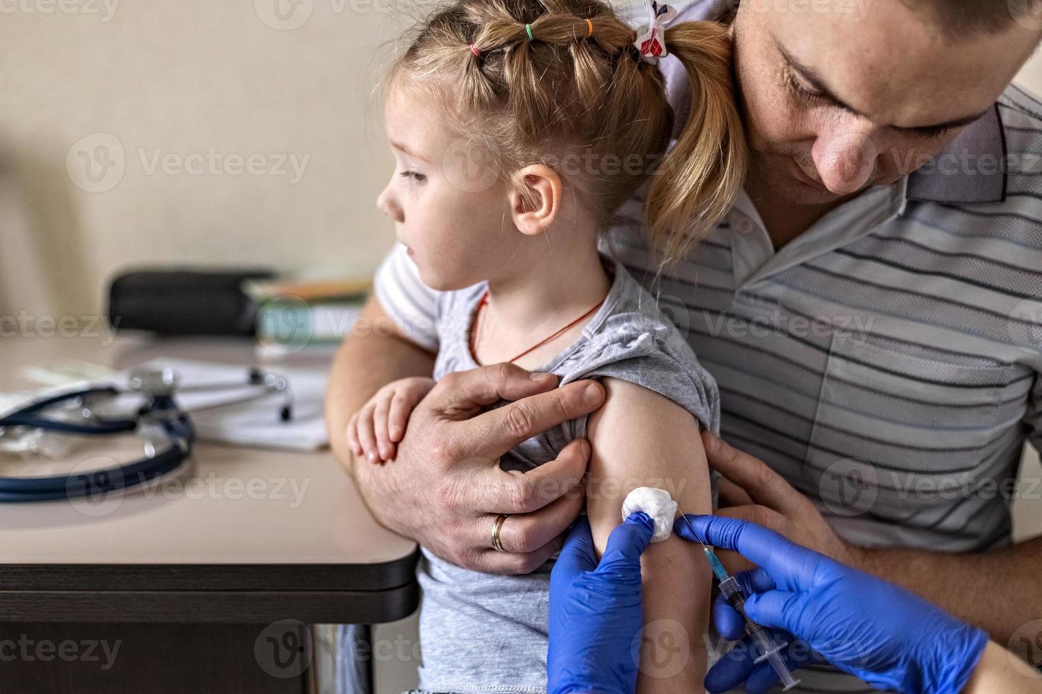 uma menina com o pai no consultório médico da clínica está sendo vacinada contra o coronavírus. o conceito de vacinação, imunização, prevenção contra covid-19. foto