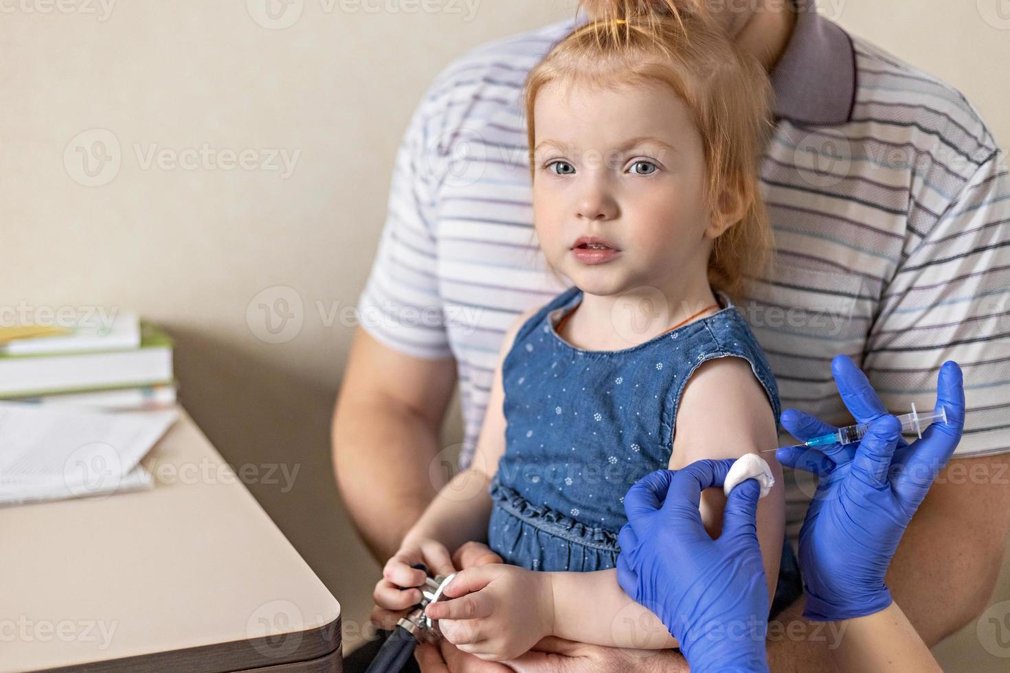 uma menina com seu pai no consultório médico da clínica está sendo vacinada contra o coronavírus. o conceito de vacinação, imunização, prevenção contra covid-19. foto