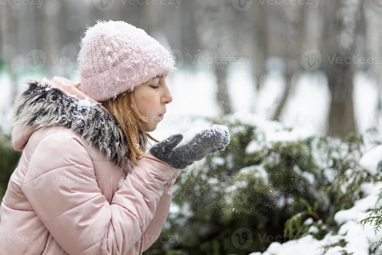 mulher feliz em um dia nevado de inverno no parque, vestida com roupas quentes, limpa a neve de suas luvas foto