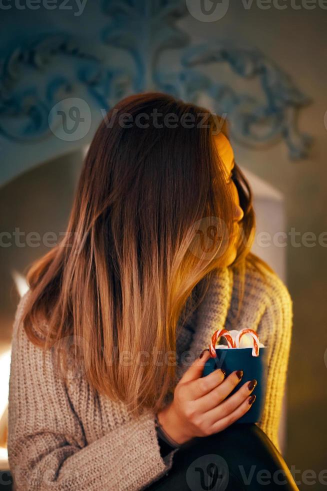 mulher de suéter com uma xícara de chocolate quente junto à lareira. foto