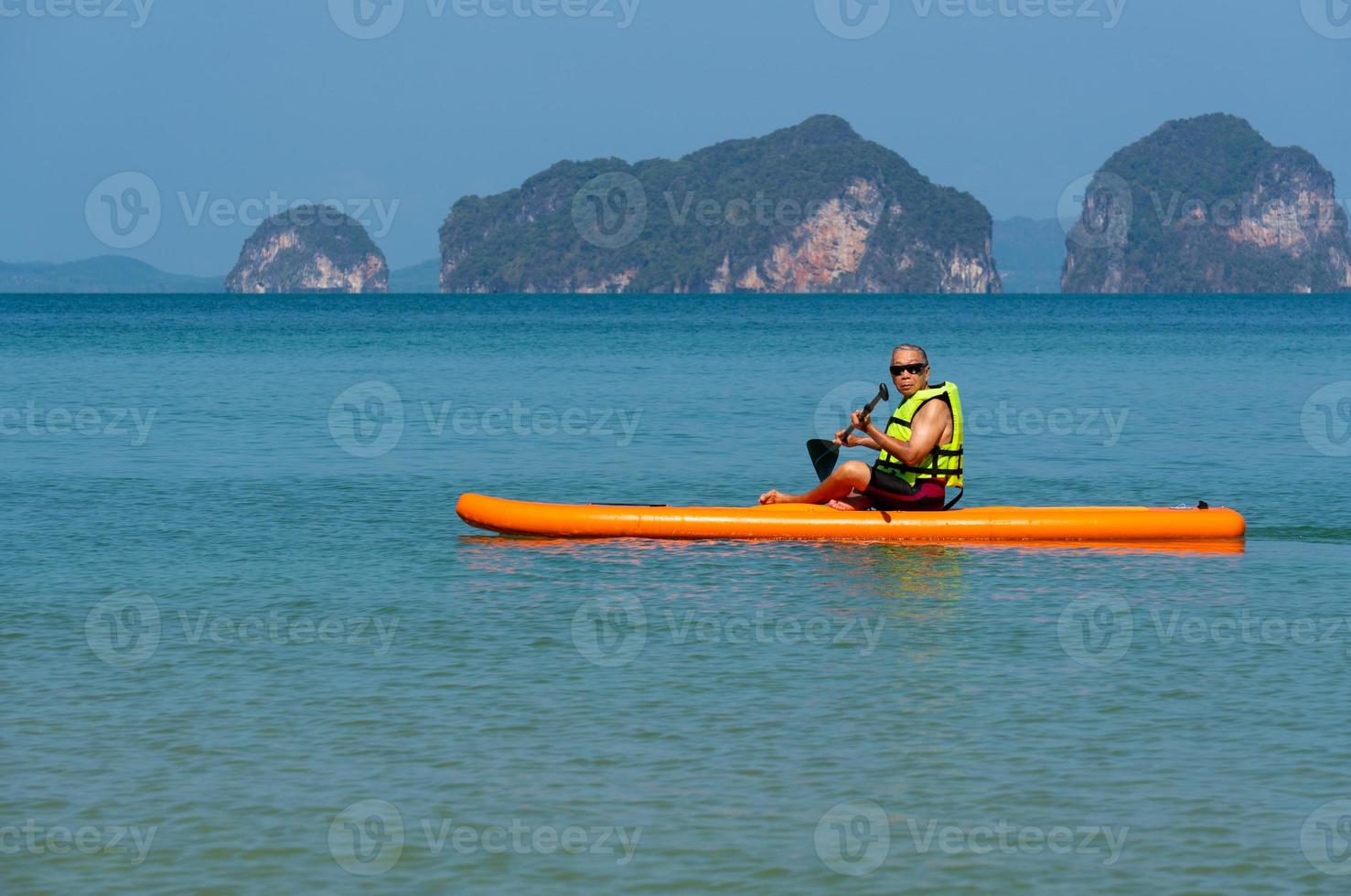 sênior homem asiático jogando paddle board no mar azul durante as férias de verão foto