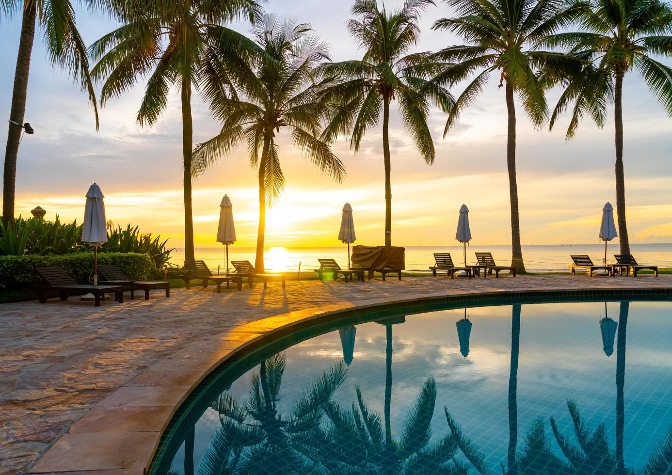 guarda-chuva e cadeira ao redor da piscina em hotel resort com nascer do sol pela manhã foto