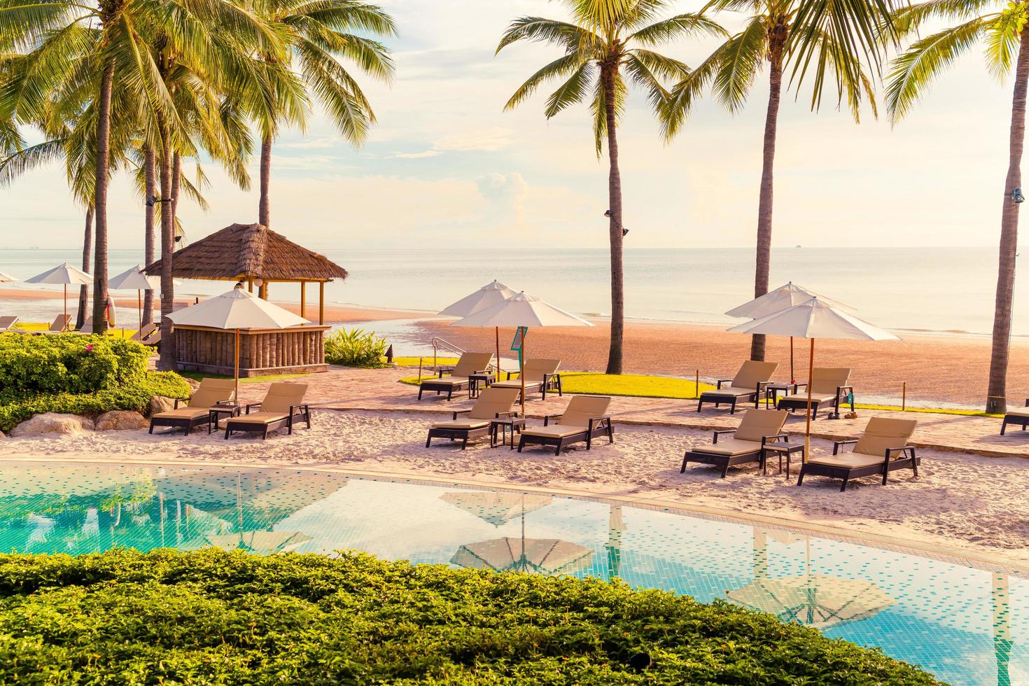 belo guarda-sol de luxo e cadeira ao redor da piscina ao ar livre em hotel e resort com coqueiro no céu do pôr do sol foto
