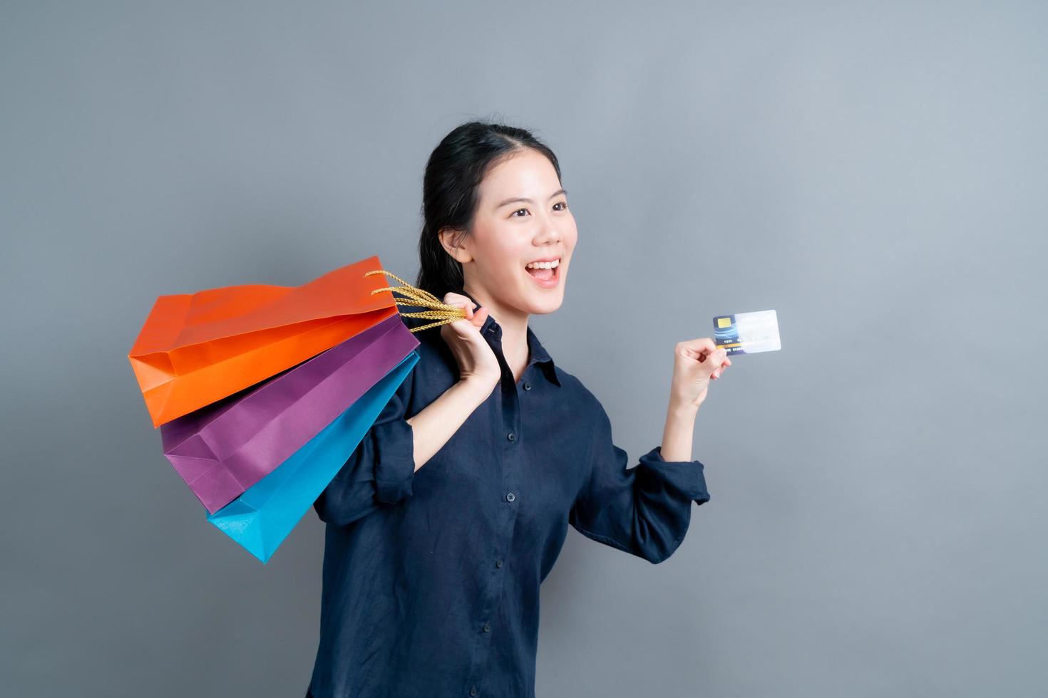 linda mulher asiática com sacolas de compras e apresentando cartão de crédito foto