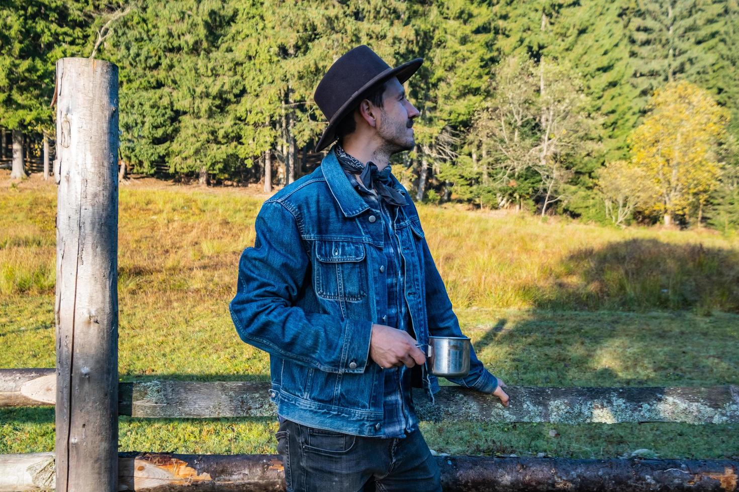 cowboy de jaqueta jeans e chapéu perto da cerca nas montanhas foto