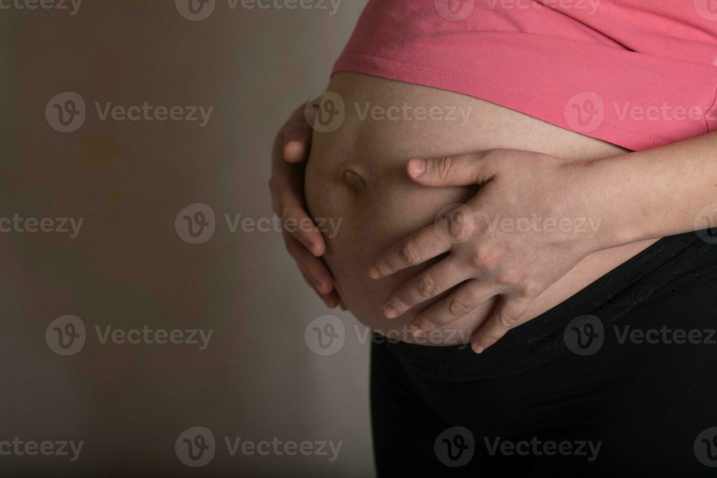 jovem grávida mulher toques dela barriga. dramático claro. foto