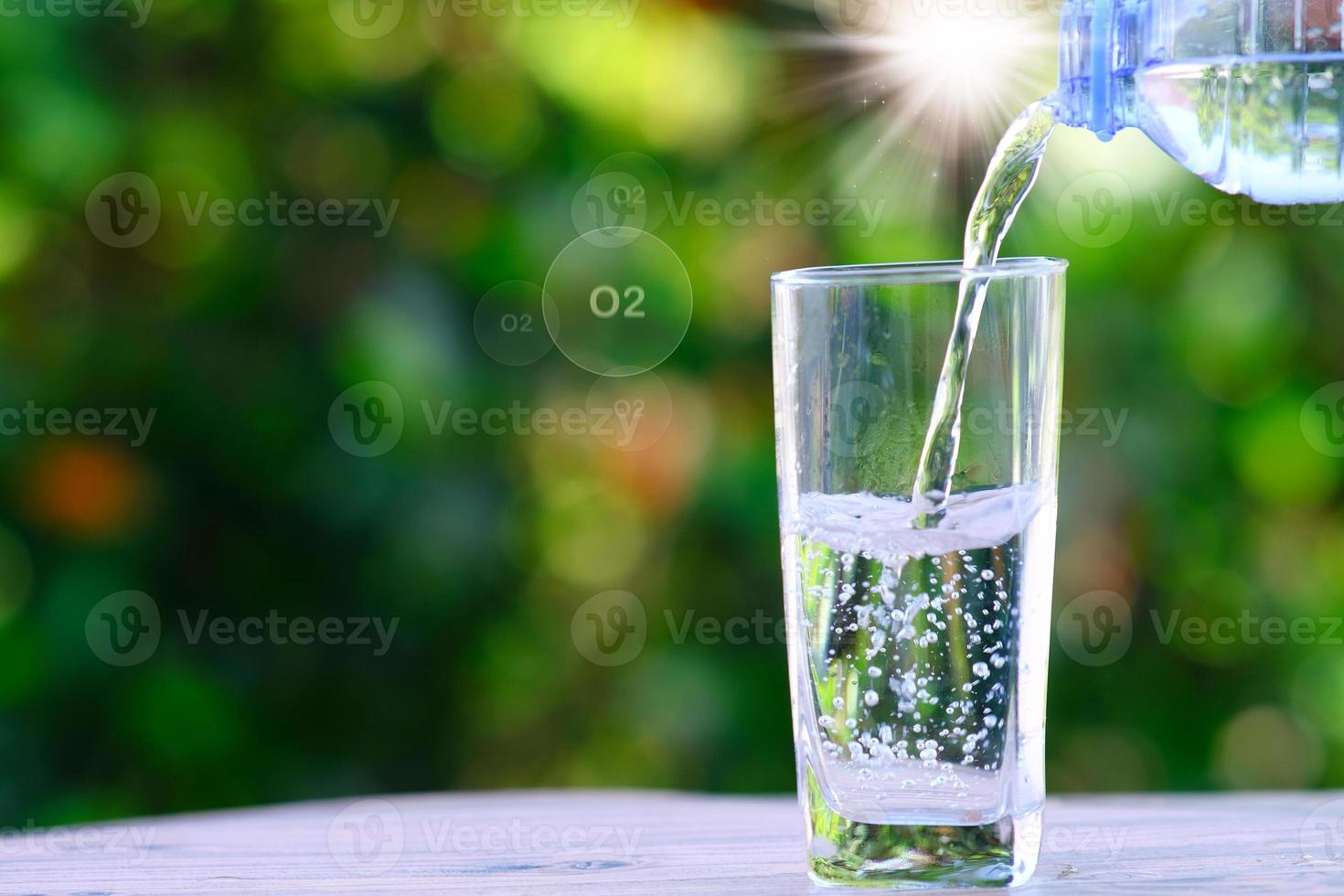 água da garrafa derramando em vidro na mesa de madeira e o conceito de saúde de água mineral, espaço para texto foto