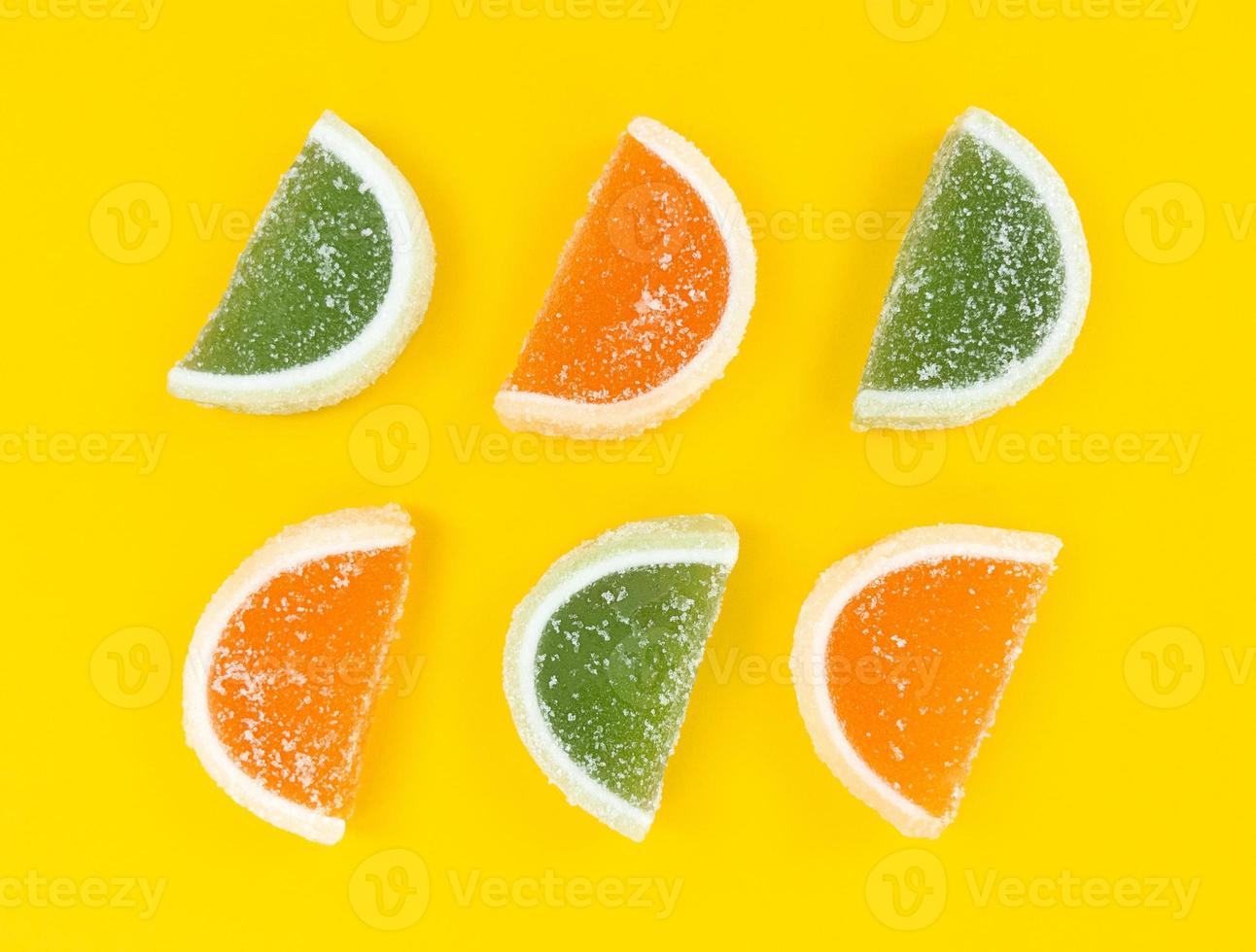 fatias de frutas cítricas geléia de laranja e verde no açúcar em fundo amarelo. foto