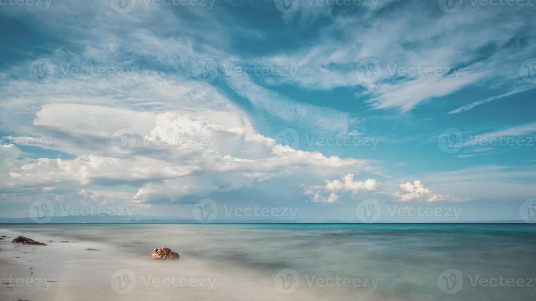 paisagem de areia e costões rochosos. bela vista do mar nublado ao pôr do sol e água do movimento borrado. foto