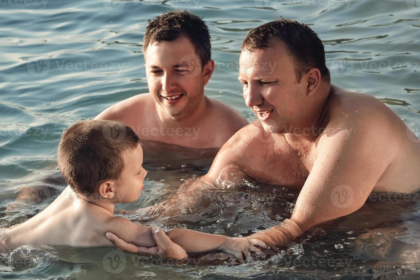 dois homens aprendem menino a nadar no mar. foto