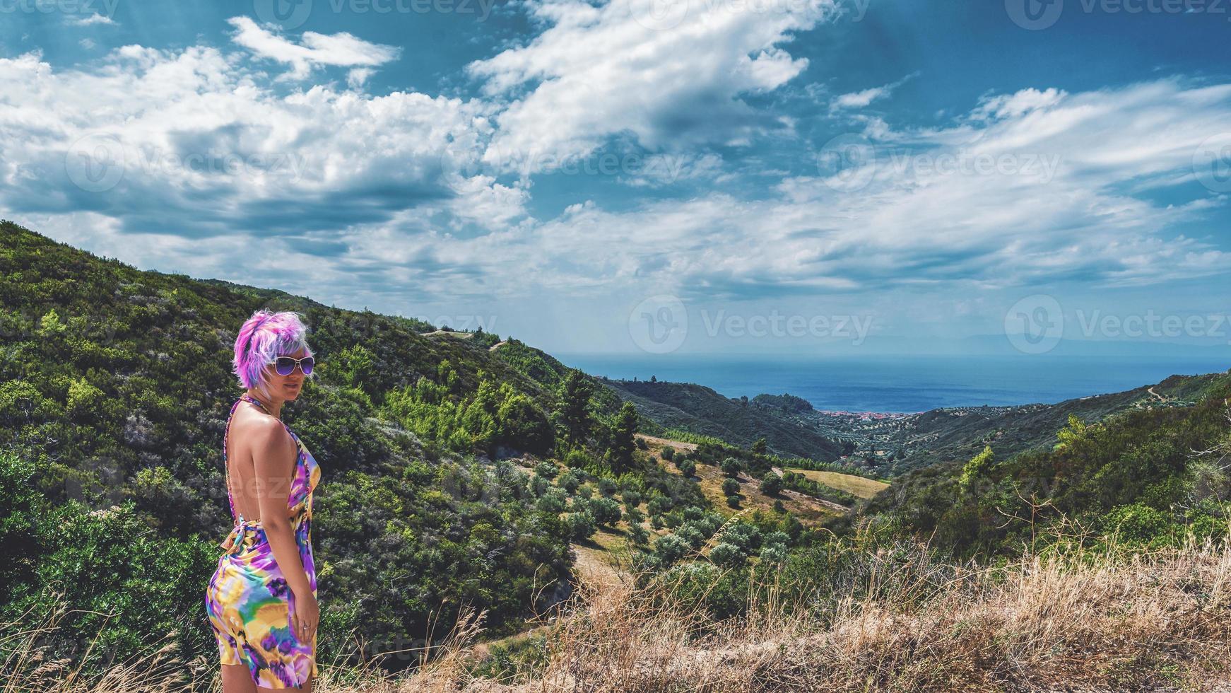 mulher com cor de cabelo rosa maluco. mulher com cabelo rosa olhando para a câmera, no horizonte vemos uma pequena cidade de nea skioni de um dos pontos mais altos da península kassandra, na grécia. foto