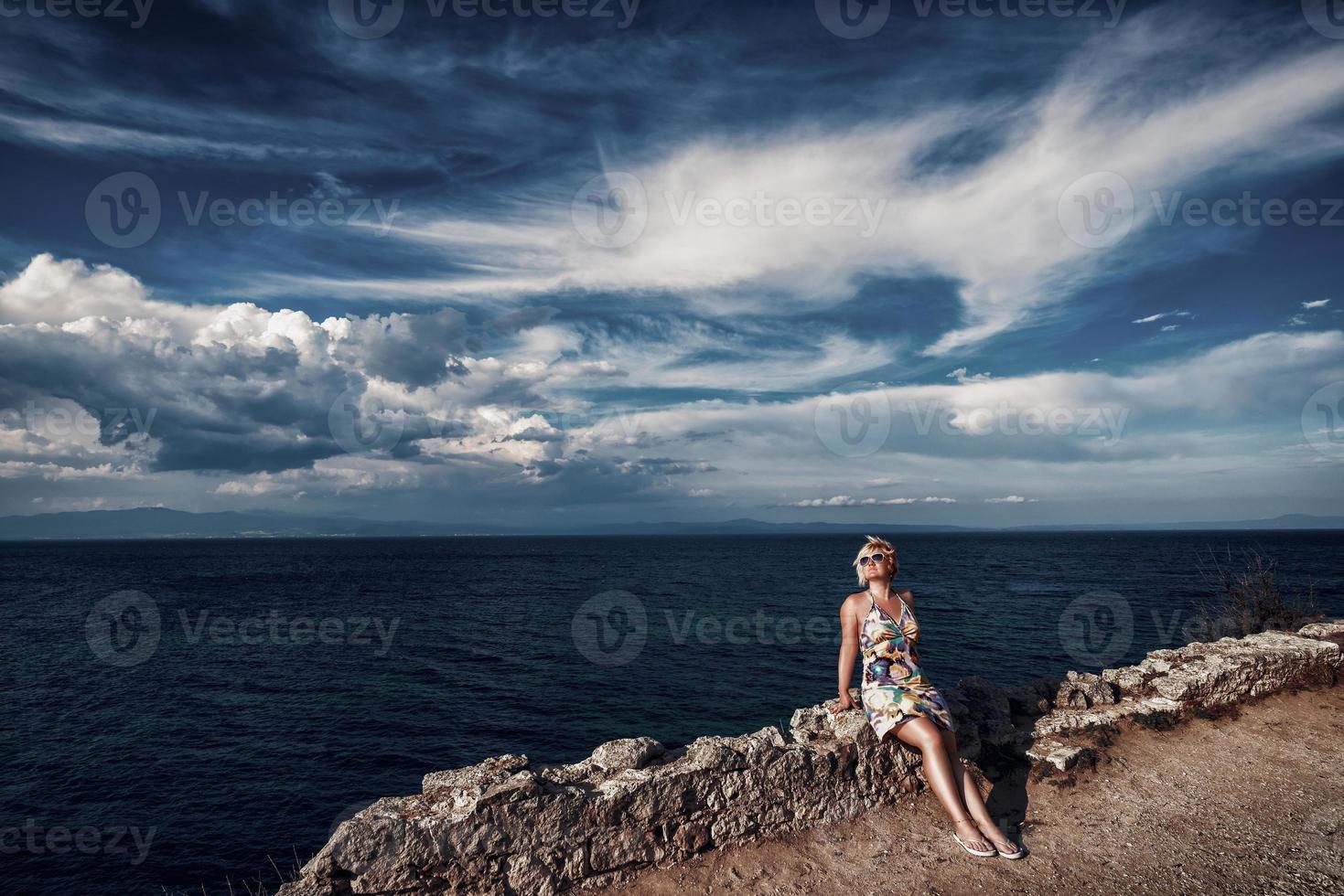 mulher loira no litoral. mulher loira atraente sentada na parede de pedra no litoral. foto