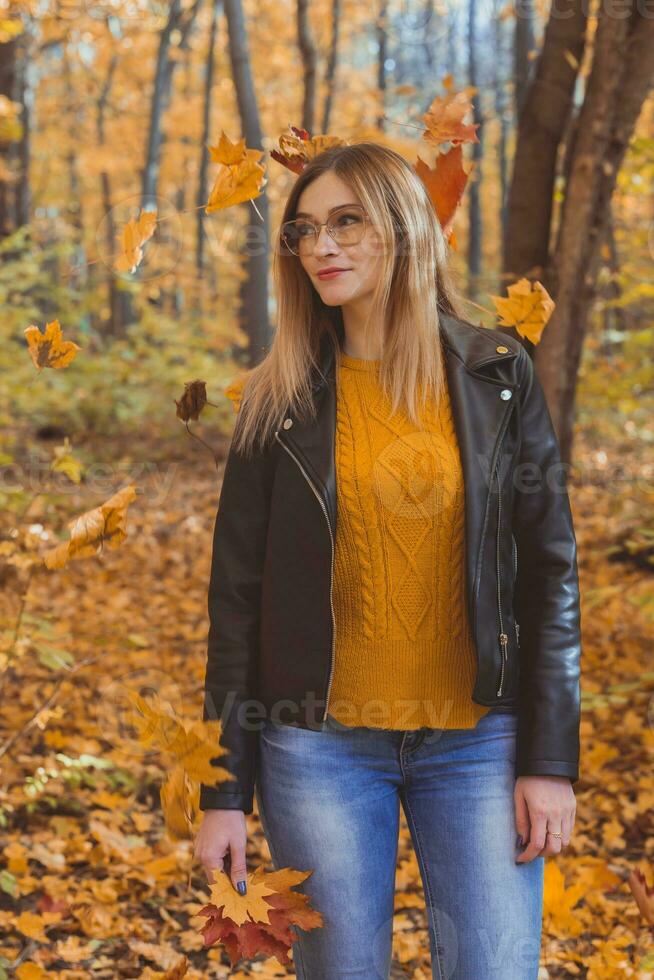 menina detém caído folhas e anda em dentro outono parque. sazonal conceito. foto