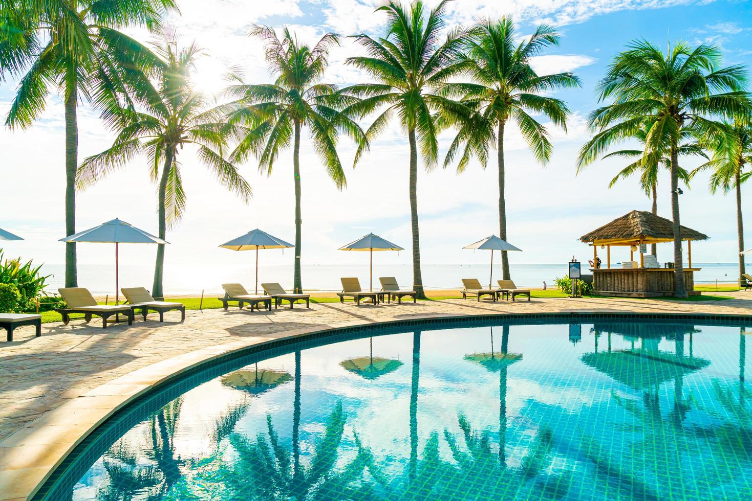 lindo guarda-sol de luxo e cadeira ao redor da piscina externa em hotel e resort com coqueiro no céu azul foto