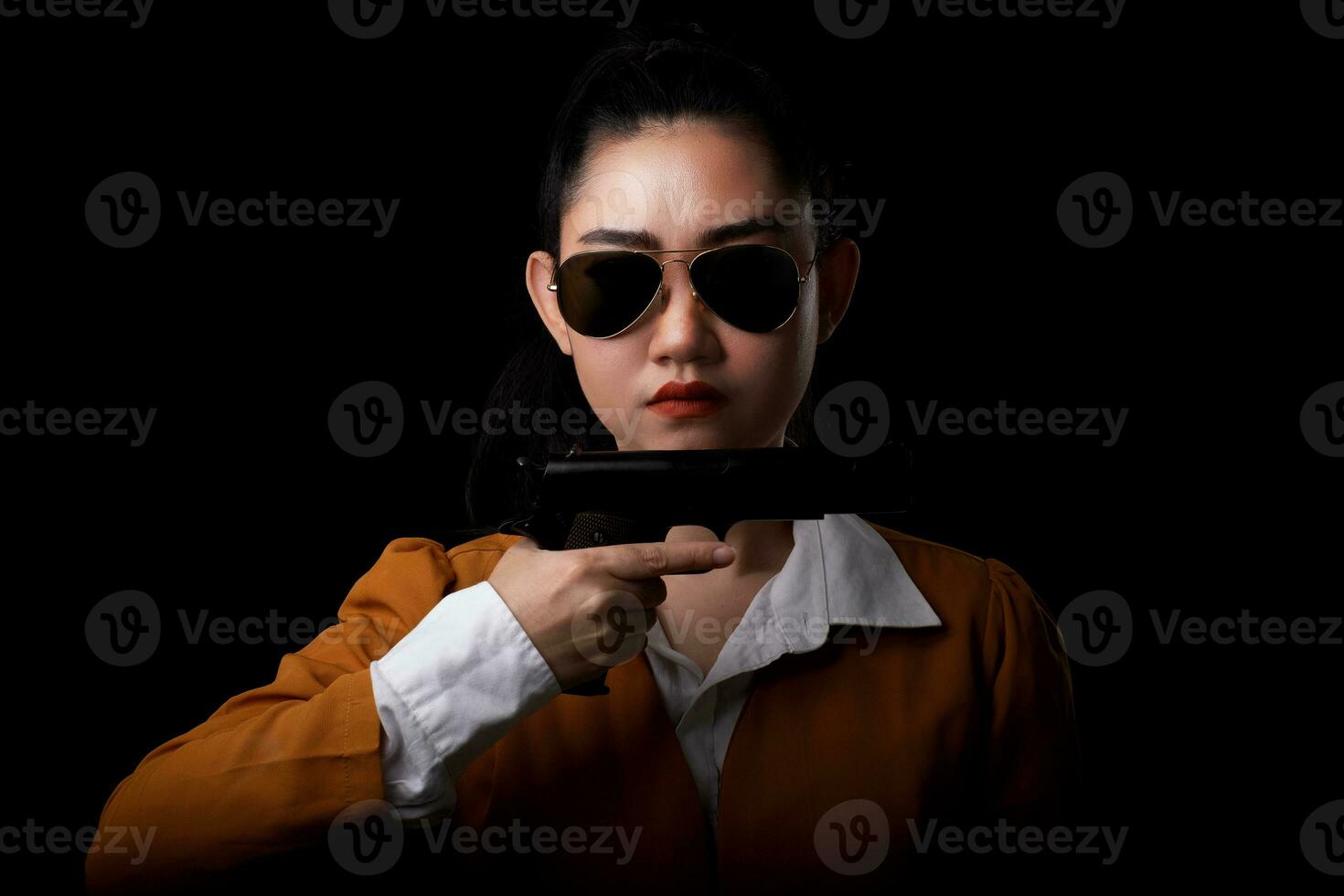 retrato linda mulher asiática vestindo um terno amarelo com uma das mãos segurando uma pistola para o fundo preto foto