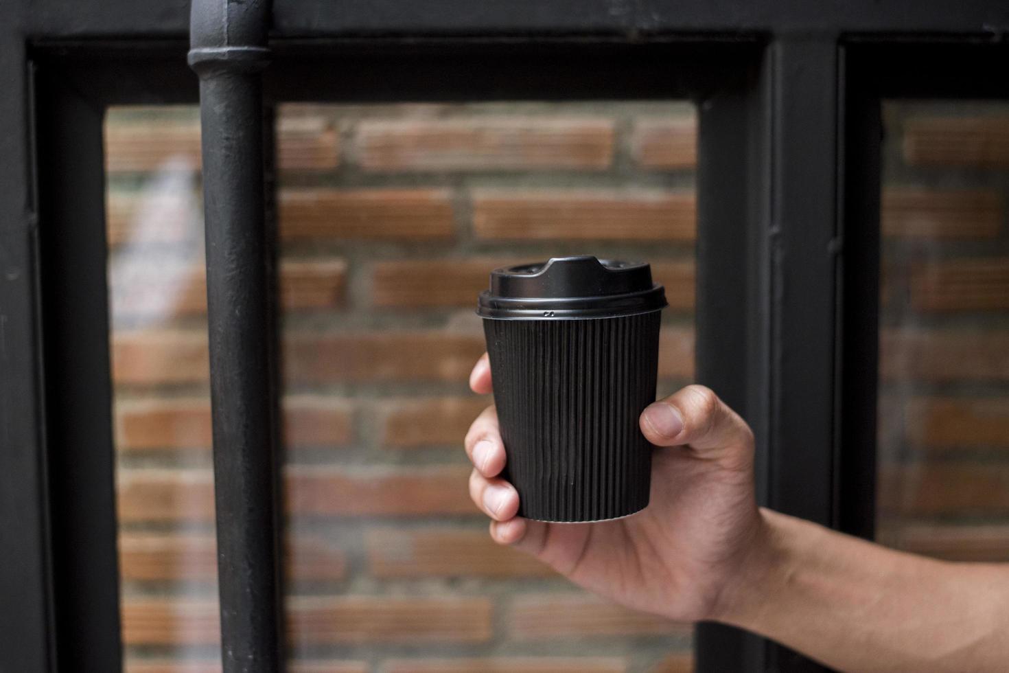 mão humana segurando uma caneca de papel de café, bebida matinal foto