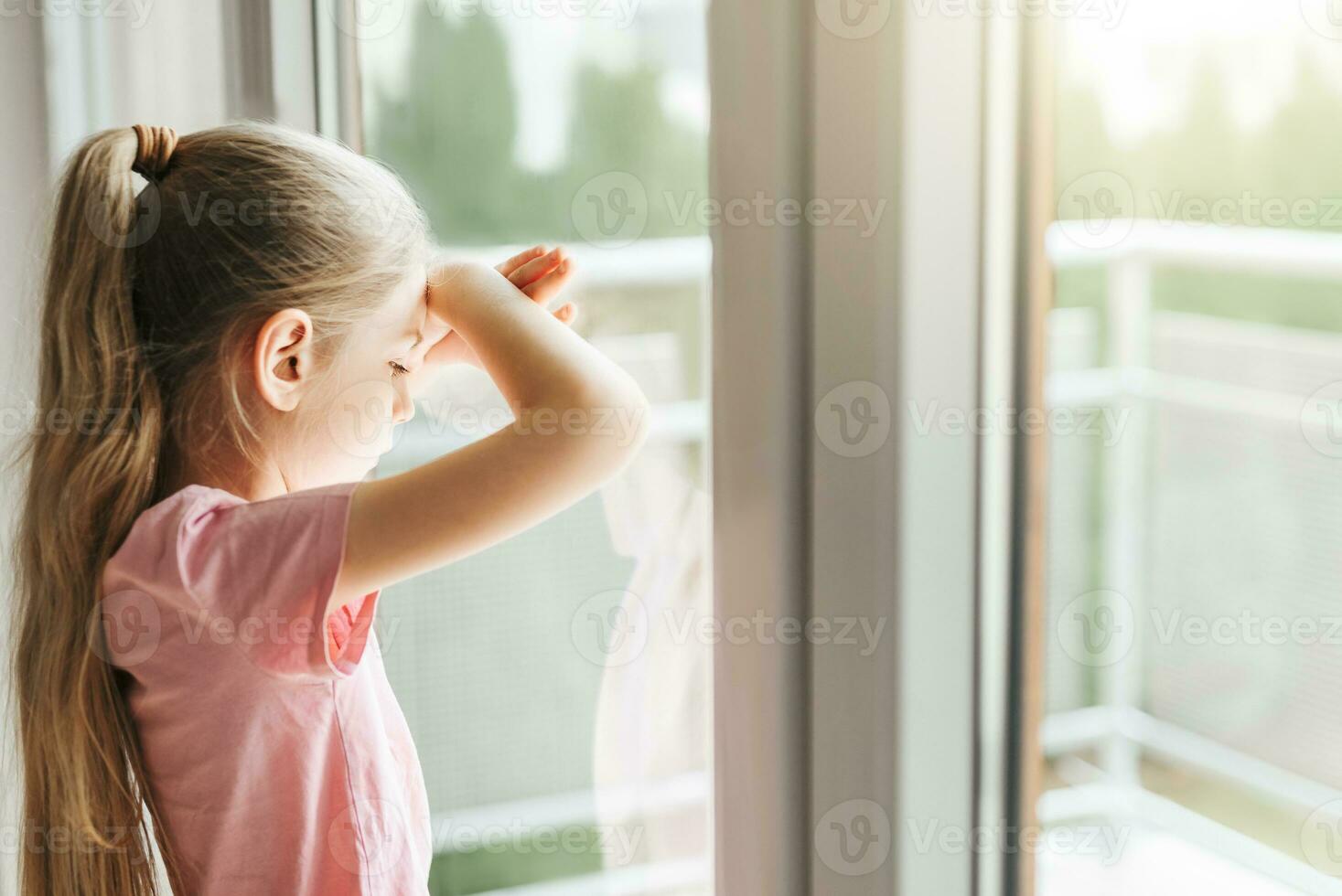 triste pequeno menina olhando através janela às lar. foto