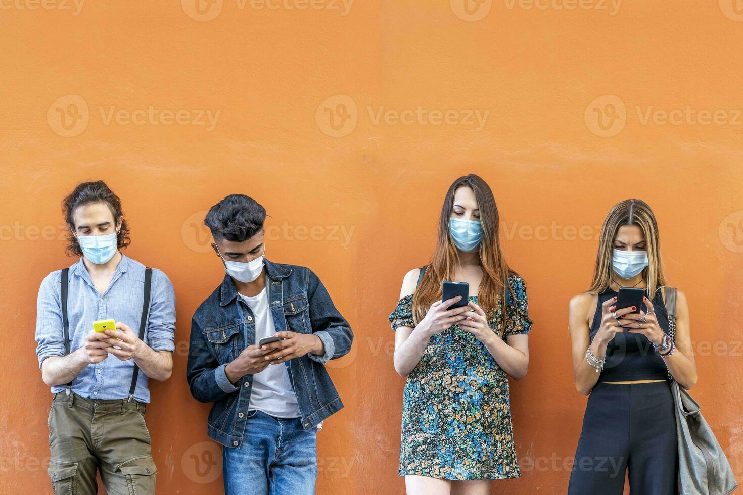 grupo do multirracial amigos com face máscaras dentro frente do laranja parede foto