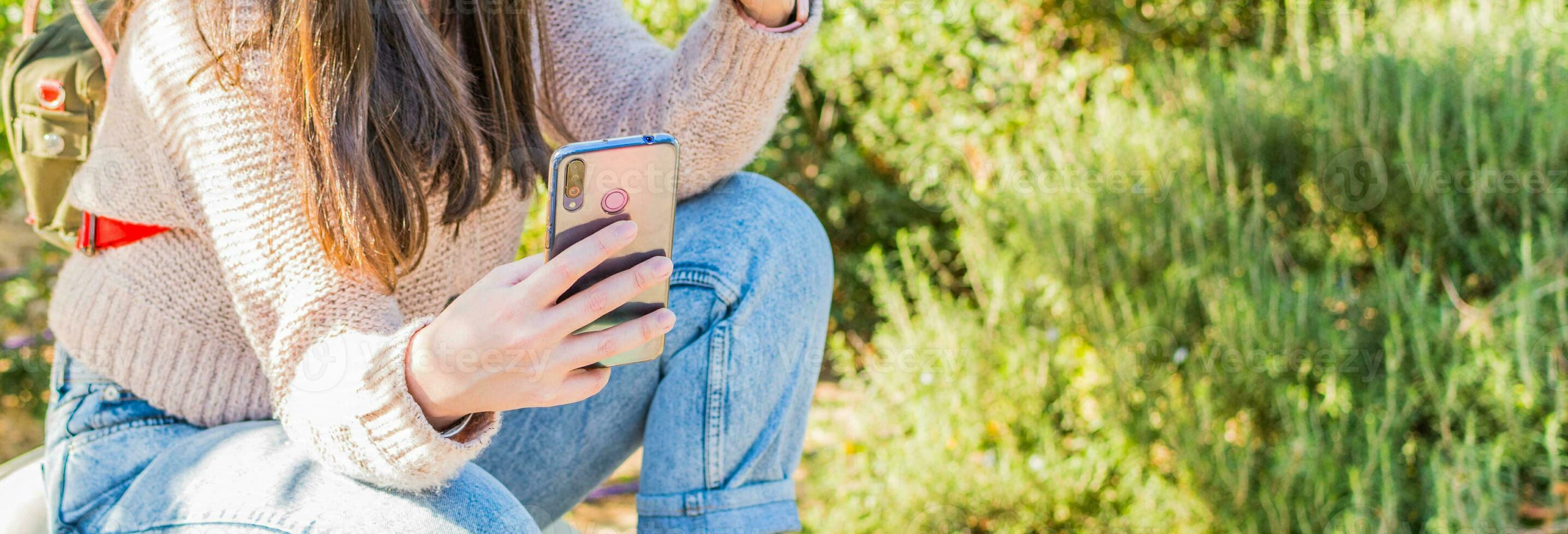 mulher mão segurando uma célula telefone, dentro uma parque, em uma ensolarado dia. foto