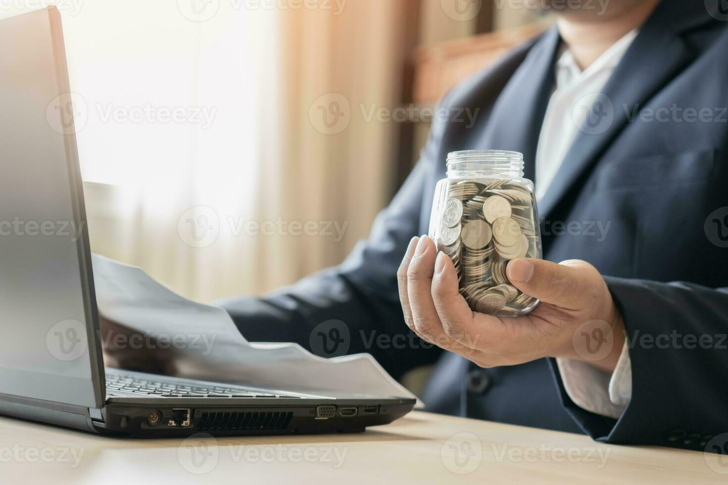 o negócio homem trabalhando com computador portátil poupança dinheiro tailandês moeda moedas dentro jarra para Novo casa. Salve  dinheiro para renda ou Comprar Novo vivo lugar. foto