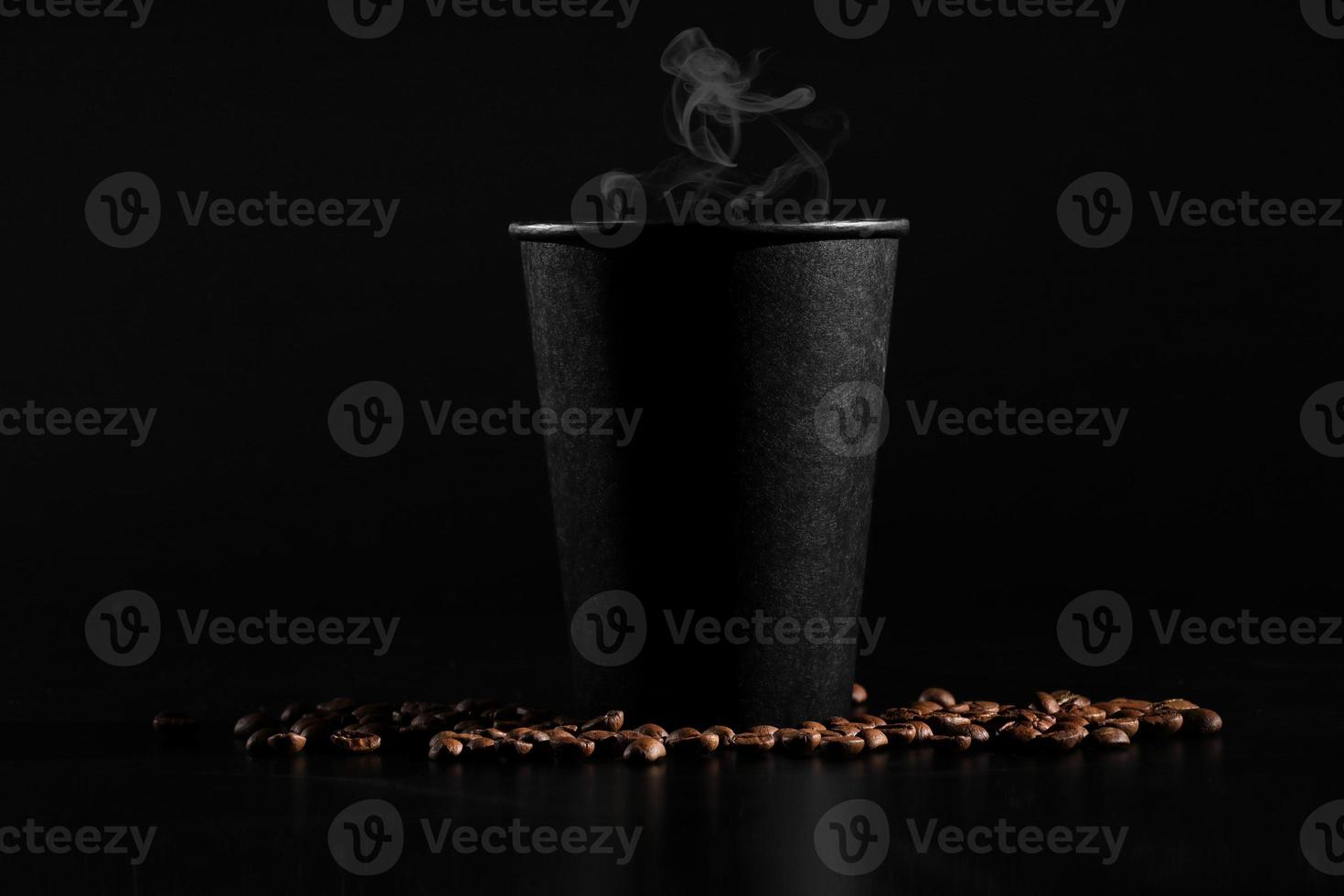 um copo preto com café quente em um fundo escuro. grãos de café espalhados. café perfumado na mesa foto