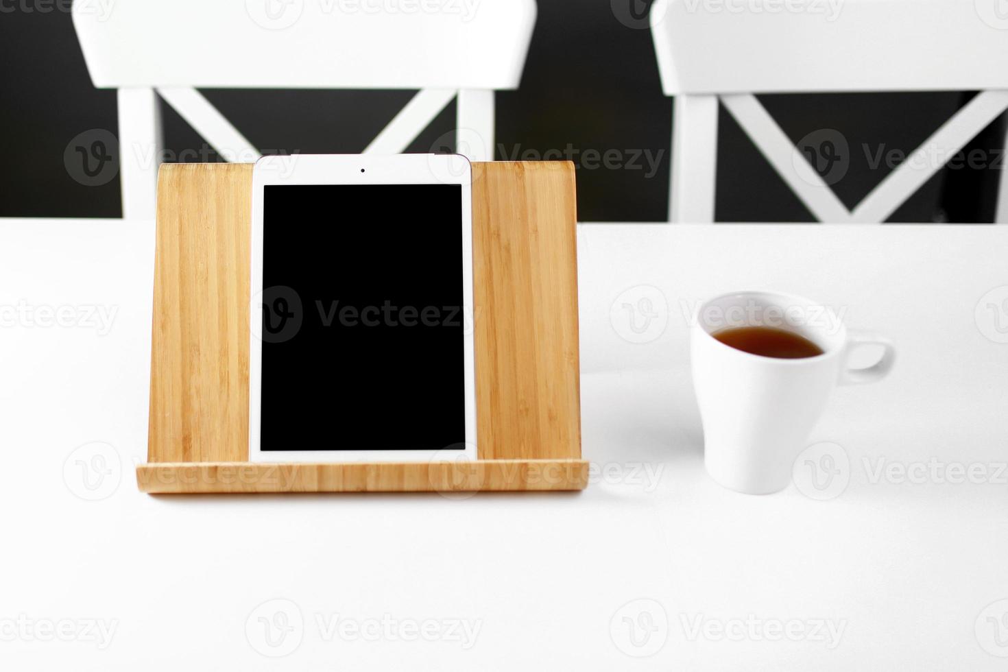 tablet digital de maquete no suporte de madeira. tablet em um suporte de madeira. caneca branca com chá. local de trabalho de escritório foto