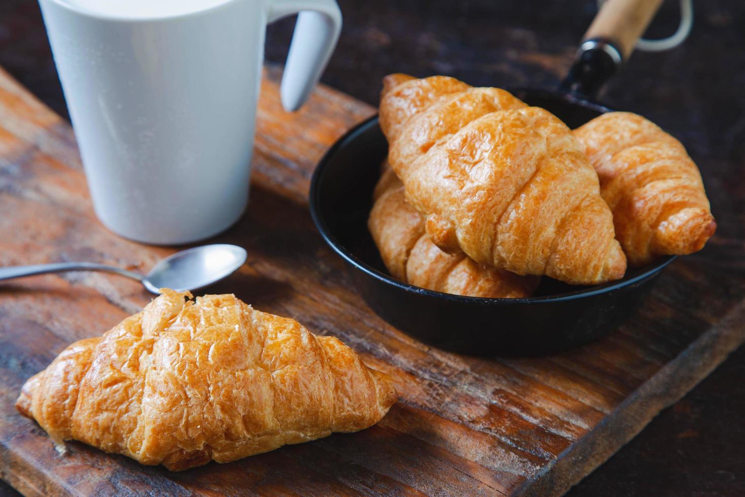 pão do café da manhã, croissants e leite fresco na mesa de madeira. foto