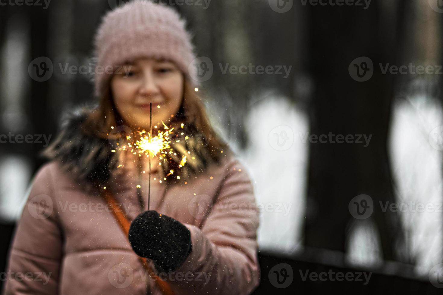 luzes de natal são respingos brilhantes queimando nas mãos de uma mulher feliz embaçada no parque. sparkler. emoções, clima de ano novo. feriados de inverno foto